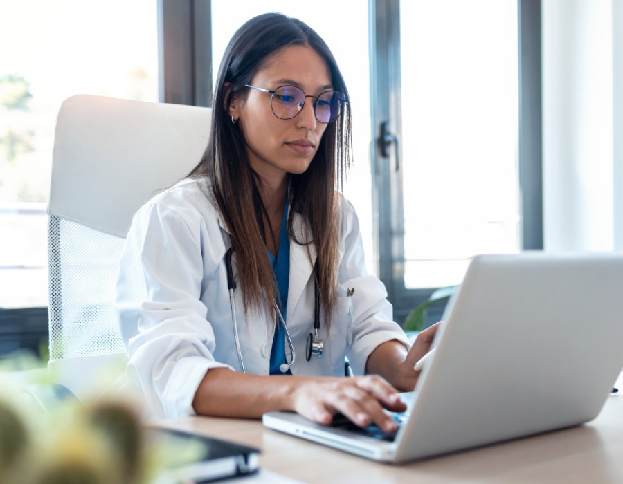 Female physician reviewing job opportunities on a laptop in a clinical office setting