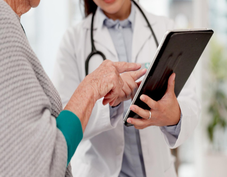 Nurse practitioner reviewing patient information on a tablet while consulting with an elderly patient in a clinic setting.