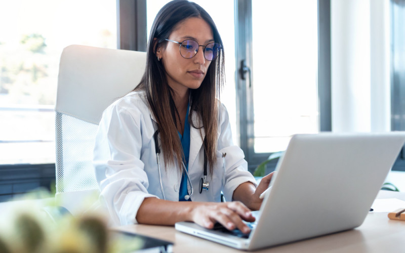 Female physician reviewing job opportunities on a laptop in a clinical office setting