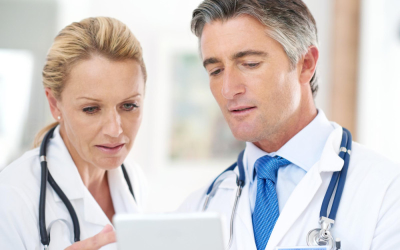 Two healthcare professionals in white coats reviewing information together on a tablet, representing clinical decision-making and career evaluation in healthcare